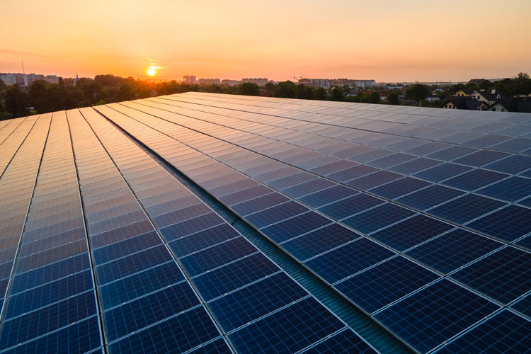 Blue photovoltaic solar panels mounted on building roof for producing clean ecological electricity at sunset. Production of renewable energy concept.